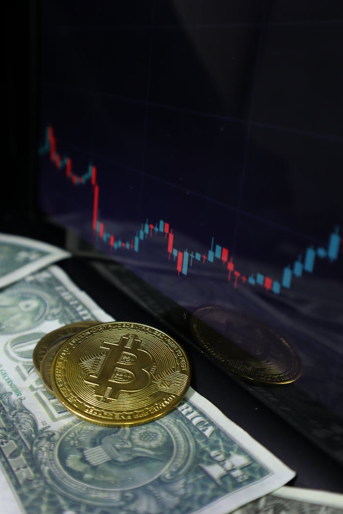 A close-up of Bitcoin coins with dollar bills and a stock market chart in the background.
